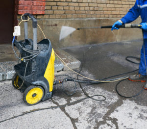 Yellow power washing machine with wand connected spraying water onto wall.